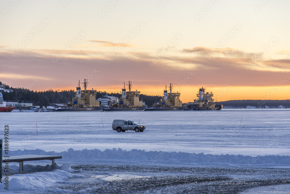 En bil kör på isen utanför Södra Hamnen i Luleå med isbrytanra vid LKAB