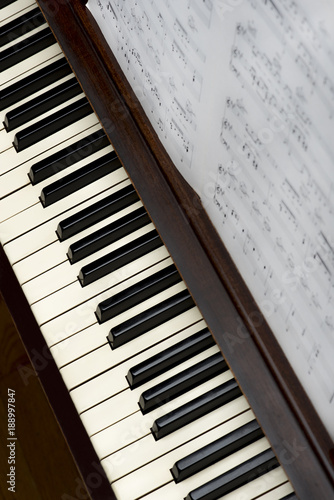 Song sheet music on wooden upright piano with white and black  keys