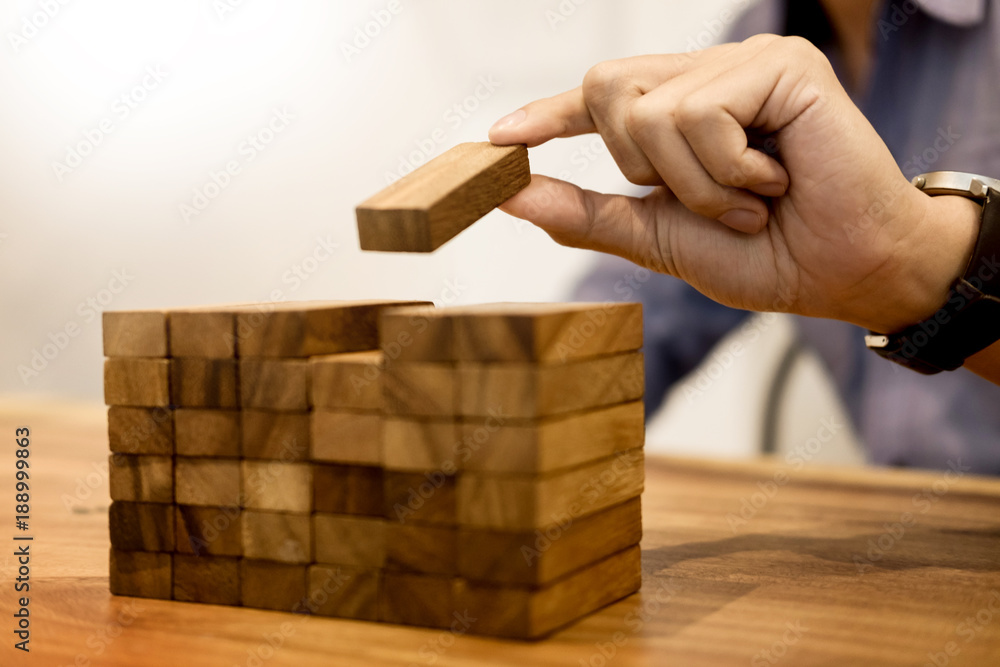 Hand of engineer playing a blocks wood tower game on blueprint or architectural project concept. Hand of engineer playing a blocks wood tower game on blueprint or architectural project concept.