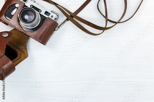 old classic photo camera in brown leather case on white wooden surface flat view
