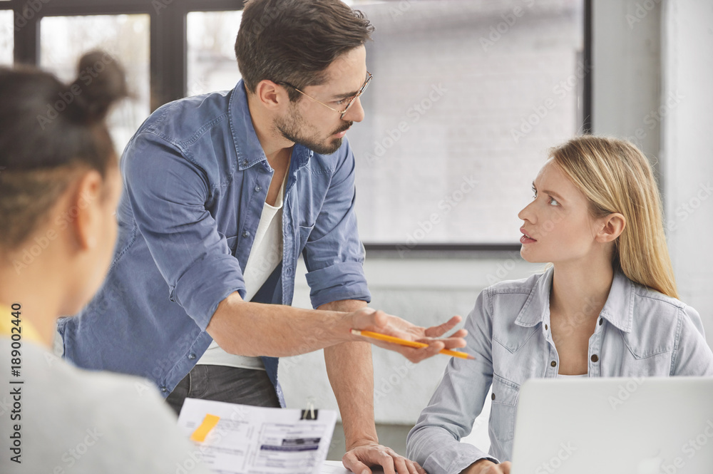 Obraz premium Portrait of skilled talented male executive director gives tasks for working day to his female employees, asks to prepare business report. Successful freelancers creat new marketing strategy