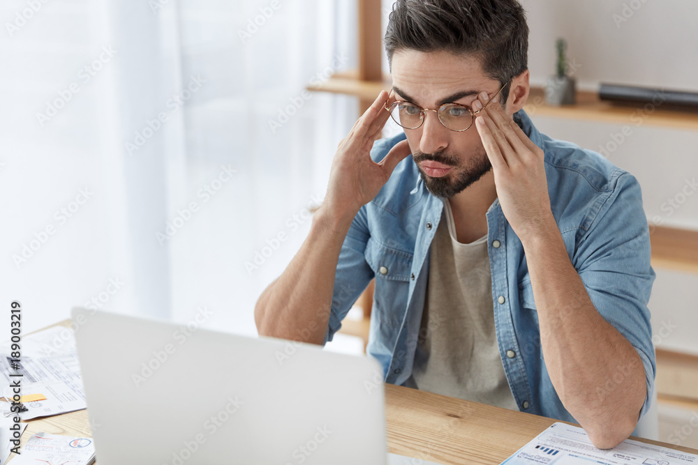 Successful bearded male IT developer thinks about creation of new program, works remotely at cabinet, has tired expression. Concentrated male writer prepares publication, tries to get inspiration Successful bearded male IT developer thinks about creation of new program, works remotely at cabinet, has tired expression. Concentrated male writer prepares publication, tries to get inspiration
