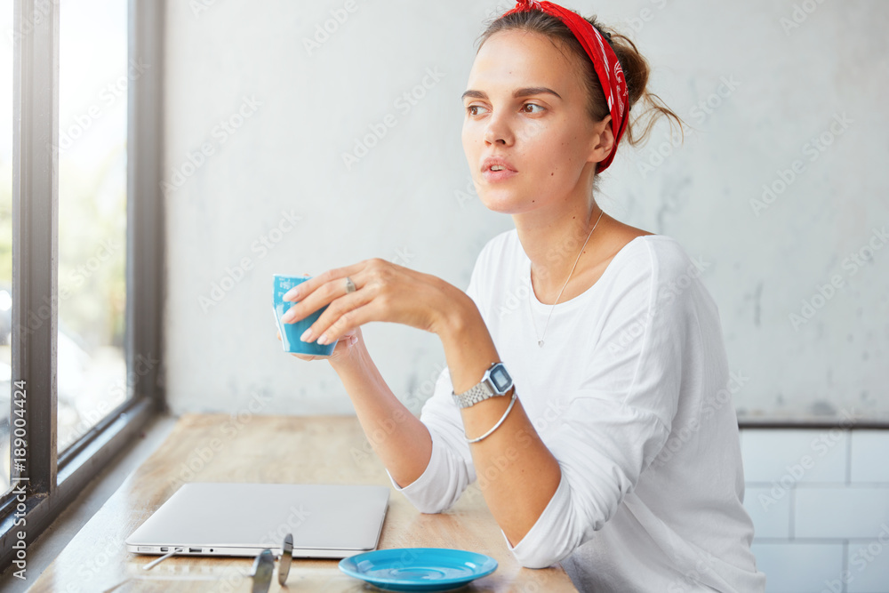 Stylish hipster girl uses laptop computer for remote work, has coffee break at coffeehouse, rests after shopping, daydreams. Charming freelancer thinks about new ideas at cafe bar, enjoys calmness Stylish hipster girl uses laptop computer for remote work, has coffee break at coffeehouse, rests after shopping, daydreams. Charming freelancer thinks about new ideas at cafe bar, enjoys calmness