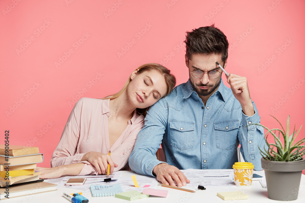 Photo of exhausted sleepy female tired after hard work on course or diploma paper, work with scientific literature. Focused brunet handsome man studies document, tries understand information Photo of exhausted sleepy female tired after hard work on course or diploma paper, work with scientific literature. Focused brunet handsome man studies document, tries understand information