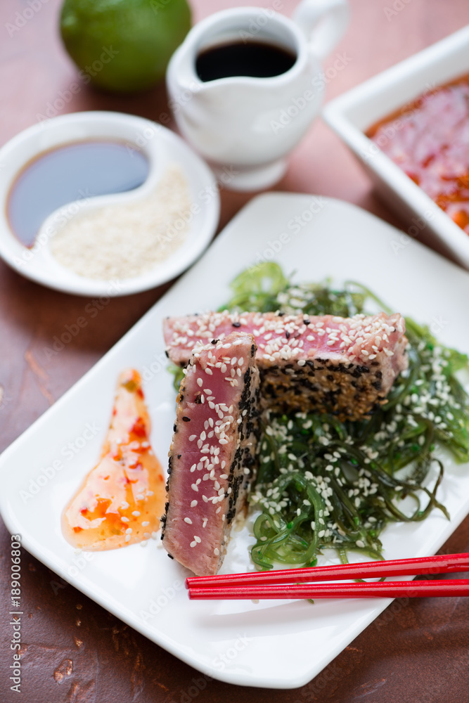Fried tuna steak on a bed of seaweed salad with sesame seeds and sauce, closeup, selective focus Fried tuna steak on a bed of seaweed salad with sesame seeds and sauce, closeup, selective focus