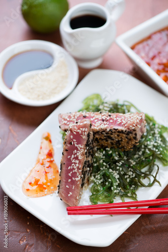 Fried tuna steak on a bed of seaweed salad with sesame seeds and sauce, closeup, selective focus