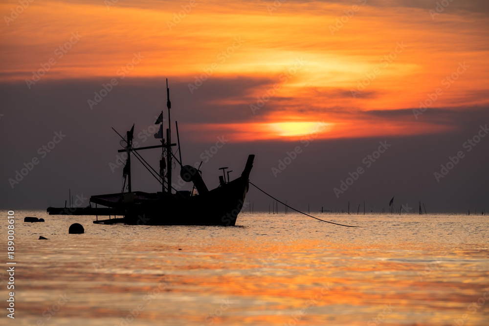 Silhouette of fisherman boat floating in the sea on dramatic sunset and sunrise sky.