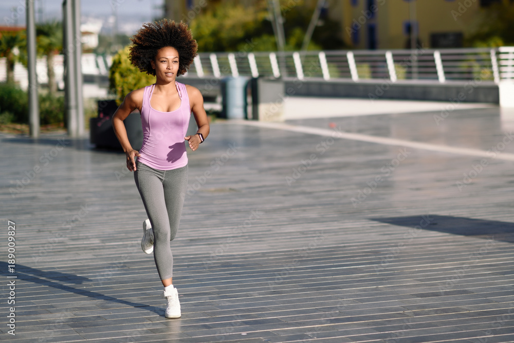 Black woman, afro hairstyle, running outdoors in urban road.