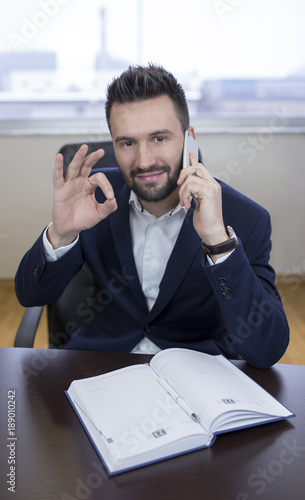Young business man showing ok and talking on phone