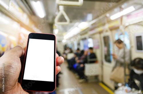 hand using mobile phone with blank screen with blurred view of people in train at train station, internet, social media technology, advertisement, marketing, commercial and network connection concept