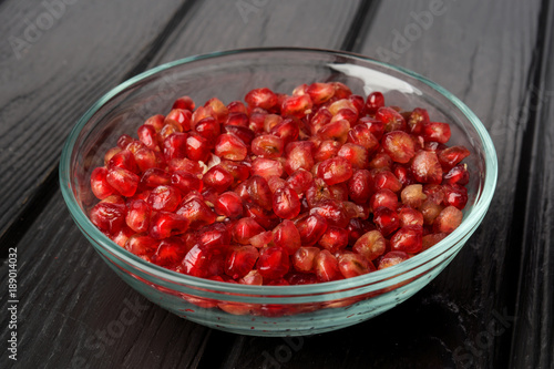 group of pomegranate grains in glass bowl on black wood