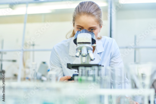 Portrait of young female scientist looking in microscope while working on medical research in science laboratory, copy space