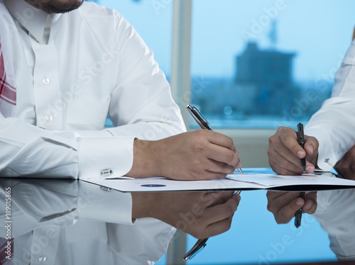 Two Saudi Businessmen Hands Signing A Ducument photo