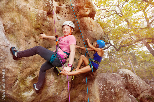 Young girl climbs a rock with female instructor