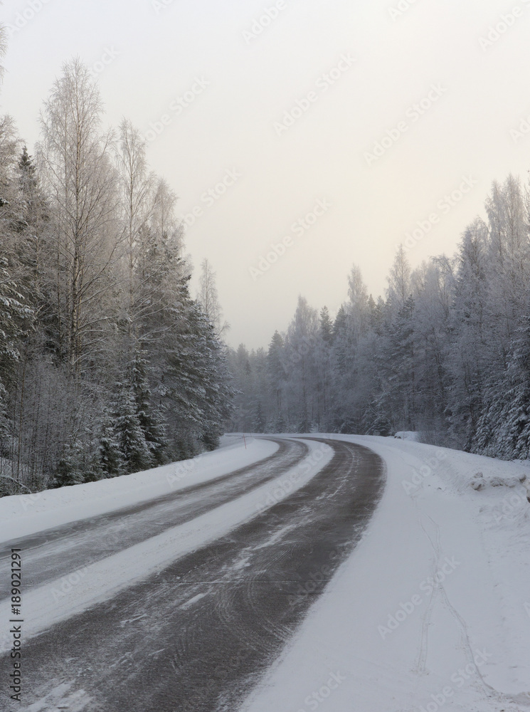 Obraz premium Winding and wintry road in Finland. Curves with snow covered asphalt road. Empty highway for traveling.