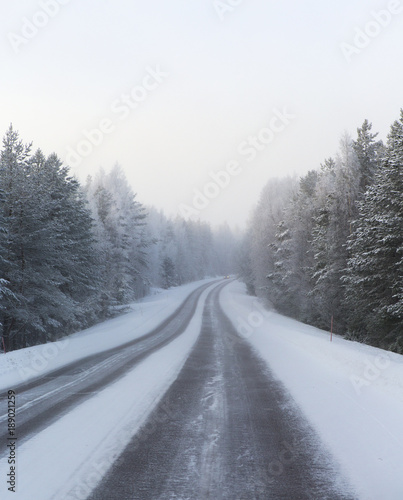 Winding and wintry road in Finland. Curves with snow covered asphalt road. Empty highway for traveling.