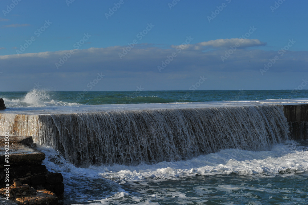 Fototapeta premium Waves breaking over coastal cliffs and breakwater during the storm, making a big splash of seawater