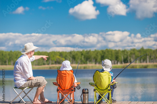 man and sons sit on the pier and fishing