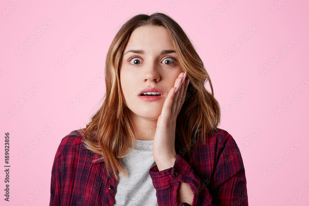 Shocked amazed female looks with eyes full of disbelief at camera, expresses great surprisment, can`t belief in such truth, poses against pink background. Human facial expressions and emotins Shocked amazed female looks with eyes full of disbelief at camera, expresses great surprisment, can`t belief in such truth, poses against pink background. Human facial expressions and emotins