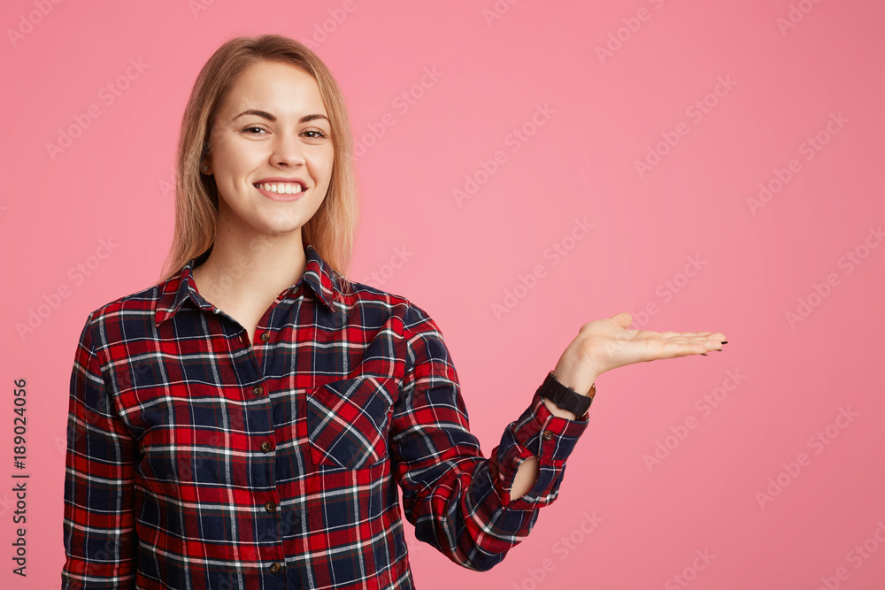 Smiling glad young female with appealing smile and charming look presents something, stratches hand aside on blank copy space for your advertising content or promotional text. Look there! Smiling glad young female with appealing smile and charming look presents something, stratches hand aside on blank copy space for your advertising content or promotional text. Look there!