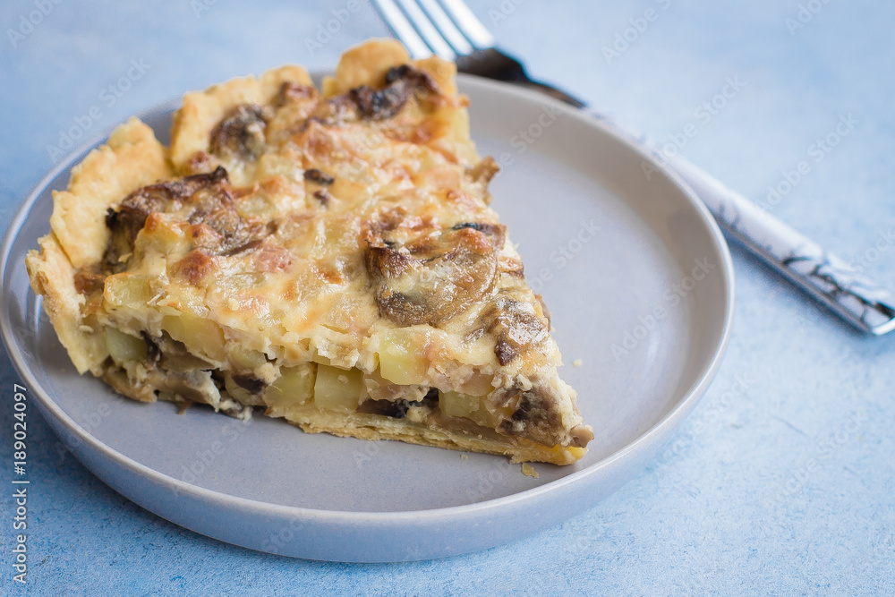 Slice of tart with mushrooms, potato and cheese on gray plate on table background. Copy space Slice of tart with mushrooms, potato and cheese on gray plate on table background. Copy space