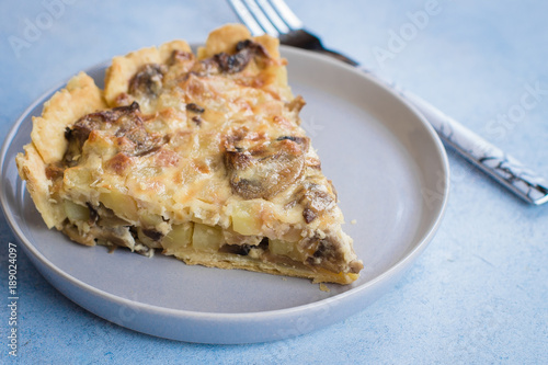 Slice of tart with mushrooms, potato and cheese on gray plate on table background. Copy space