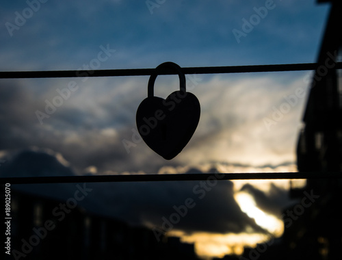 Silhouette of the heart shaped padlock hanging on the wire, with a romantic sky in the background