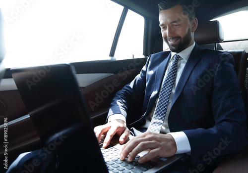 businessman sitting in the back-seat of a car, using his laptop © ASDF