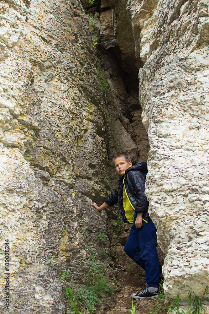 A cheerful little boy traveler stands in the crevice of the rock.