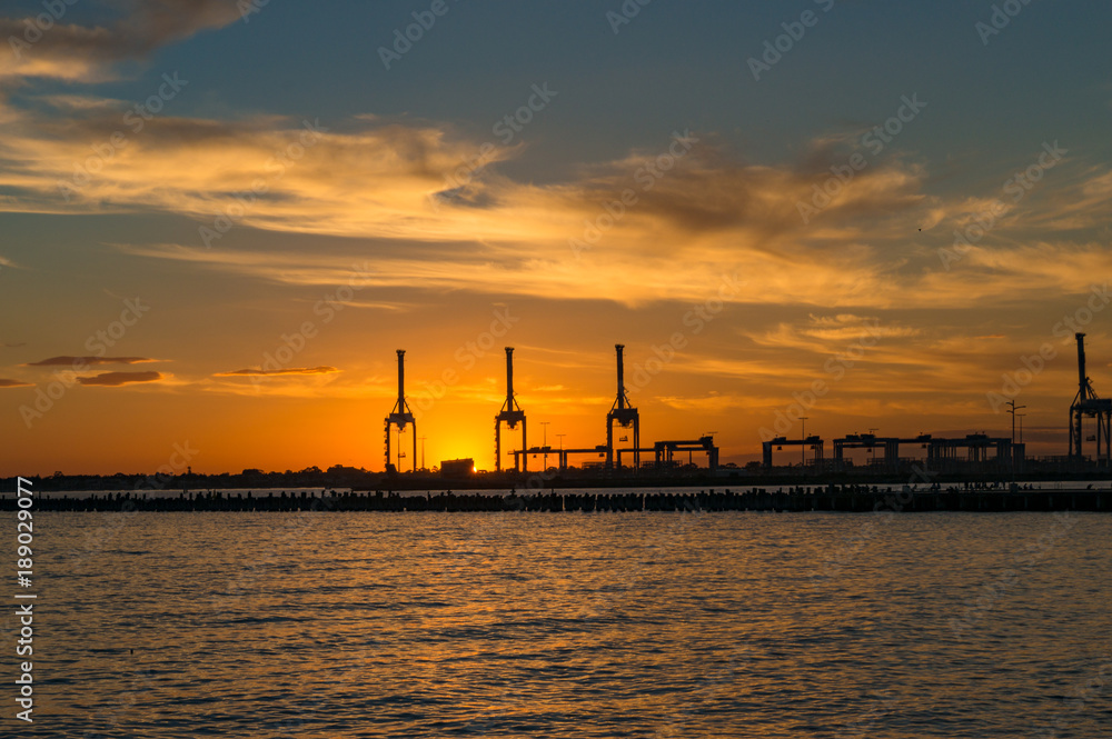 Silhouettes of industrial machines against sunset sky on the background