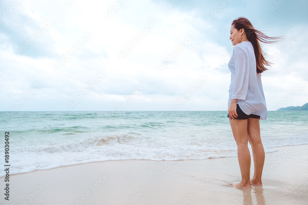 A woman standing and looking at view on the beach with the sea and blue sky background A woman standing and looking at view on the beach with the sea and blue sky background