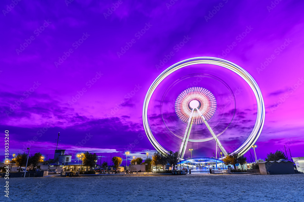 Spinning ferris wheel at sunrise blue hour in Rimini, Italy. Long exposure abstract image
