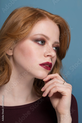 Pensive redhead girl looking to side, close-up portrait on blue background.