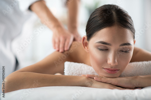 Portrait of serene young woman enjoying massage at wellness center. Her eyes are closed with satisfaction. Peace and comfort concept
