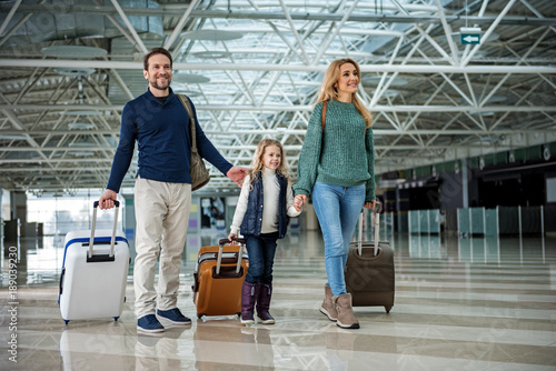 Full length of happy family walking through airport. Everyone carrying own suitcase