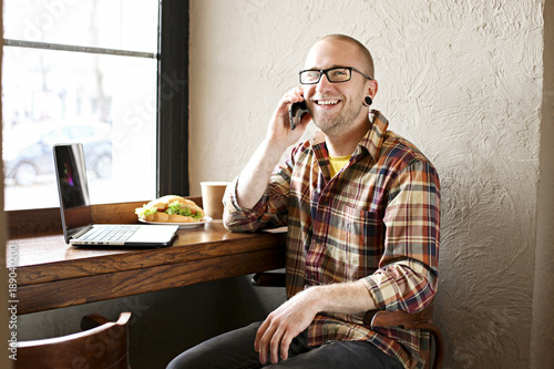 Smiling bearded businessman wearing casual hipster clothing using laptop and cell smartphone in coffe house. photo