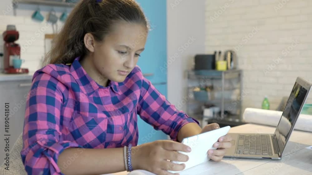 Young, teenage girl with tablet and book, learning, sitting by table in kitchen
Young, teenage girl with tablet and book, learning, sitting by table in kitchen
