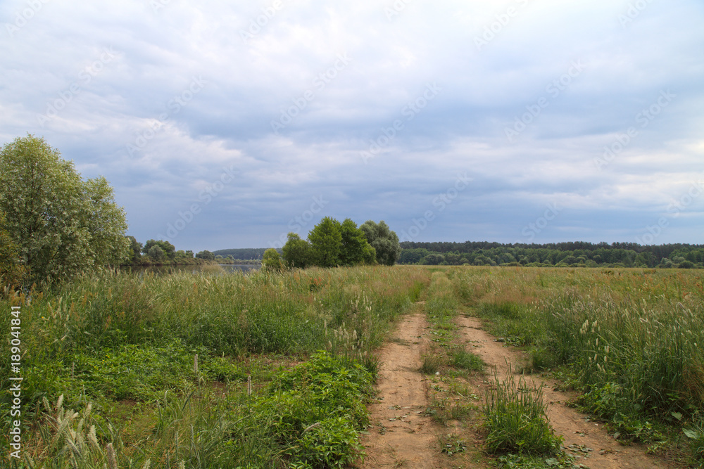 Landscape on a summer day before the rain. The Dnieper River and the road through the meadow.