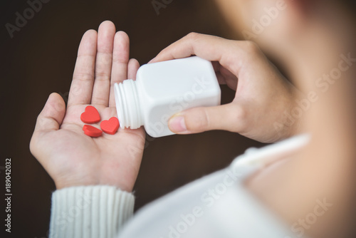 Female holding a white pill bottle and red pills in heart shape.