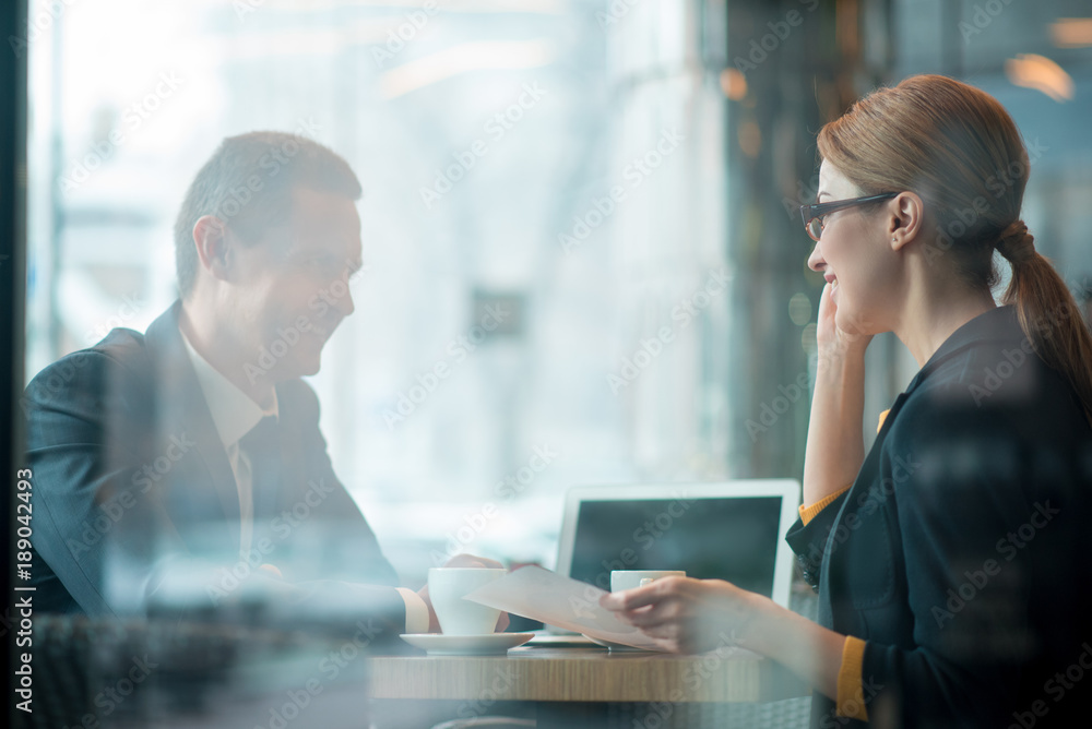 Side view smiling businessman talking with cheerful partner while situating at desk. They having job with laptop in office. Occupation concept Side view smiling businessman talking with cheerful partner while situating at desk. They having job with laptop in office. Occupation concept