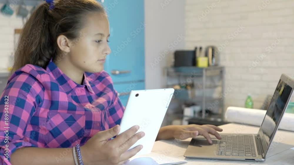 Young, teenage girl with laptop and tablet doing homework sitting by table in kitchen
Young, teenage girl with laptop and tablet doing homework sitting by table in kitchen