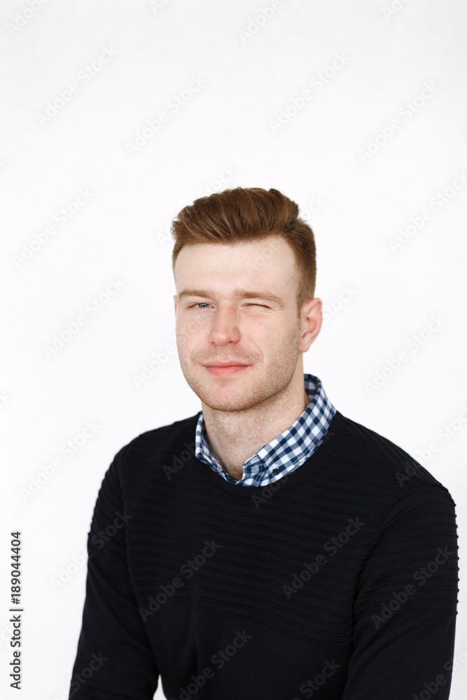 Cheerful handsome redhead young guy in black cardigan checkered shirt photographed against white wall in the studio Cheerful handsome redhead young guy in black cardigan checkered shirt photographed against white wall in the studio