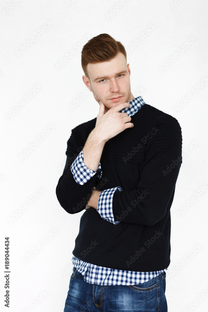 Cheerful handsome redhead young guy in black cardigan checkered shirt photographed against white wall in the studio Cheerful handsome redhead young guy in black cardigan checkered shirt photographed against white wall in the studio