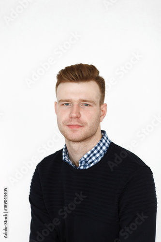 Cheerful handsome redhead young guy in black cardigan checkered shirt photographed against white wall in the studio © sergeyzapotylok