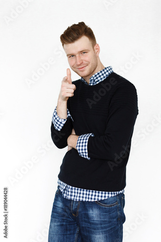 Cheerful handsome redhead young guy in black cardigan checkered shirt photographed against white wall in the studio