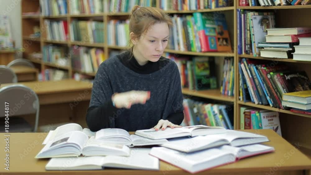 A young woman in the library reads a lot of books. She is terrified by the amount of information. Student reading book surrounded by lot of books/I will never make it too much to study A young woman in the library reads a lot of books. She is terrified by the amount of information. Student reading book surrounded by lot of books/I will never make it too much to study