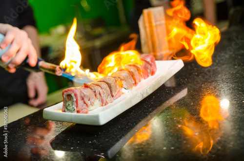 Man's hand holding torch burner. Chef prepares sushi.