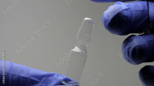 A man in blue latex gloves holds ampoules with a clear solution for injections. Close up view