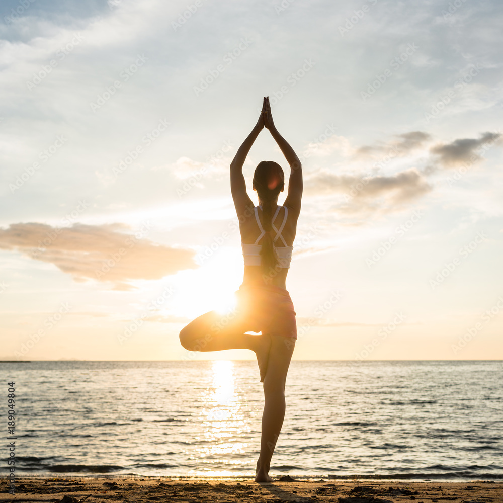 Silhouette of a woman practicing the tree yoga pose on a beach at ...