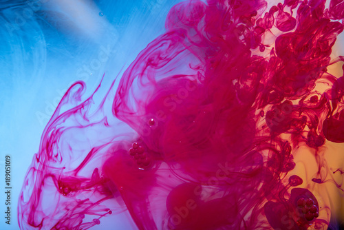 Swirls of red paint moving in the water like smoke on a blue background. Abstract background